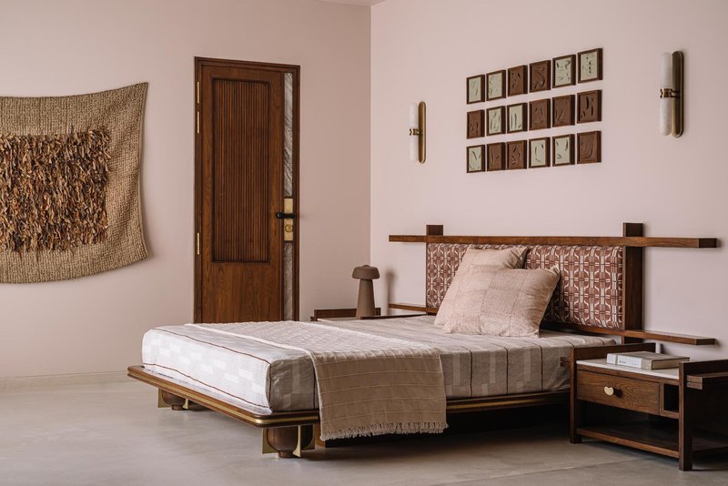 Bedroom with low platform bed, woven wall hanging and grid of framed artworks in natural light