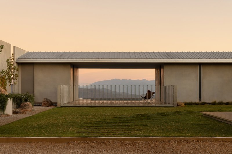 Garden view of the linear pavilion with corrugated metal roof and glazed opening framing distant mountains at dusk
