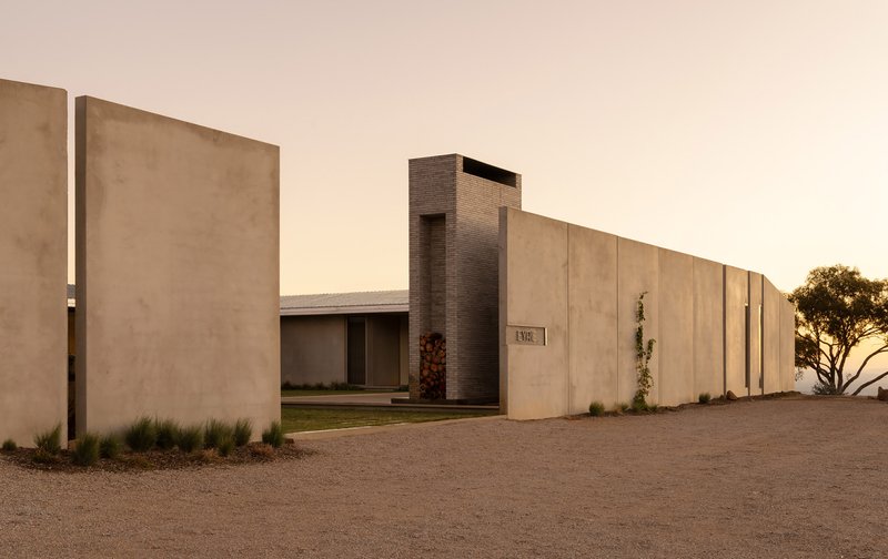 Street view of paneled concrete perimeter wall with brick chimney tower at golden hour