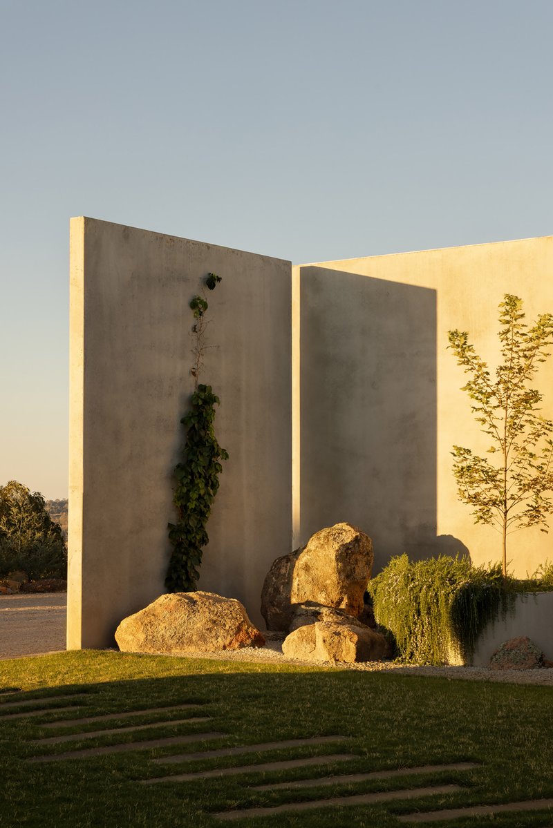 Concrete entry walls with recessed lighting flanking boulders and plantings at sunset