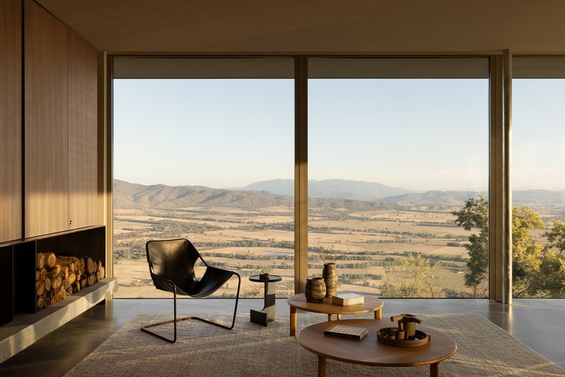 Interior living space with floor-to-ceiling glazing and fireplace overlooking the valley landscape in warm afternoon light