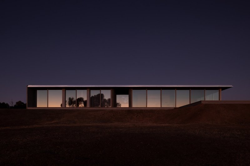 Long glazed facade illuminated from within at twilight against the dark hillside and deepening blue sky