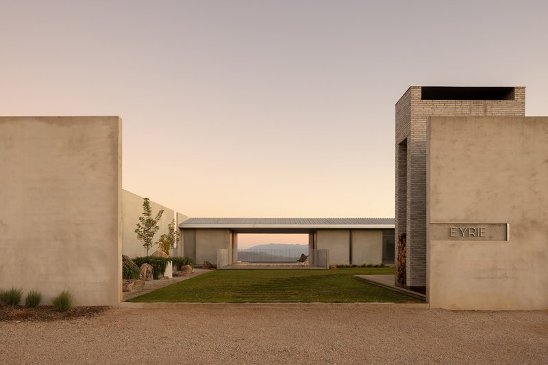 Entry courtyard framed by rammed earth walls and brick chimney with view through to mountains at sunset
