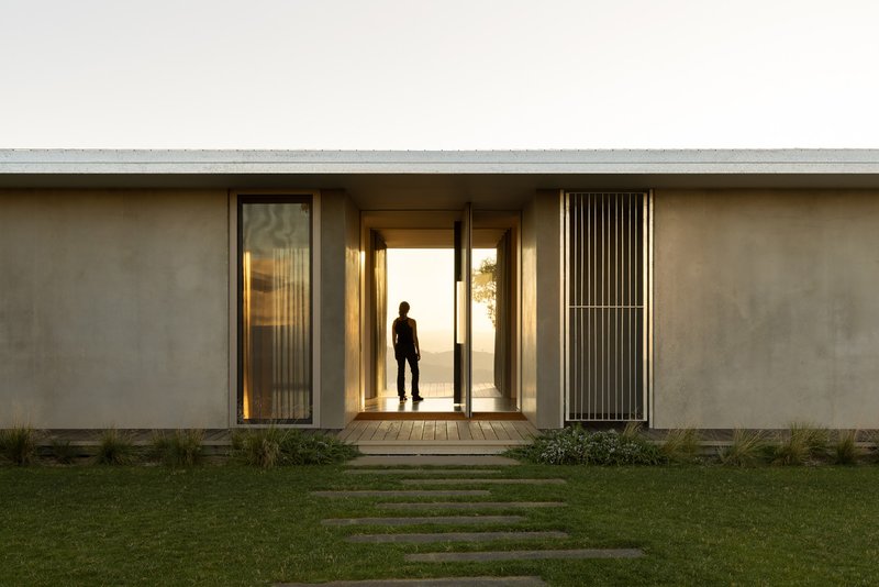 Entry facade with timber deck and concrete stepping stones crossing a lawn at dusk
