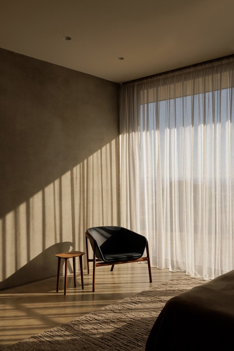 Interior corner with sheer curtains casting striped shadows across the timber floor