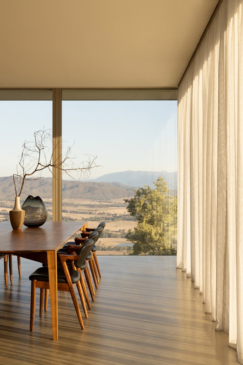 Dining area with timber floor and sheer curtains overlooking a valley landscape at dusk