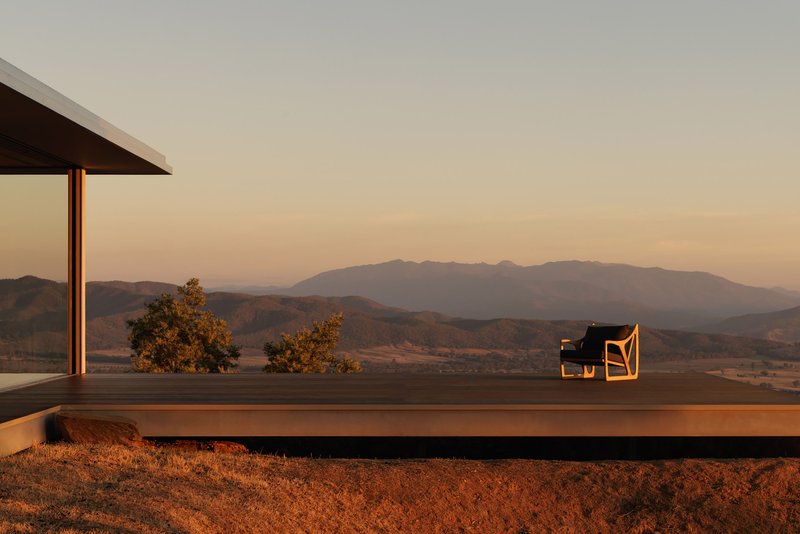 Cantilevered terrace with timber decking and a single chair overlooking rolling hills at sunset