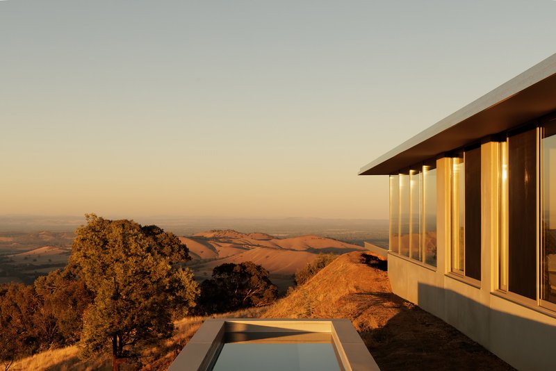 Corner view showing flat roof overhang, vertical window slots, and reflecting pool at dusk