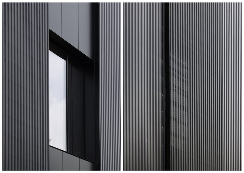 Close-up of vertical metal cladding with an angled window opening framed in dark panels