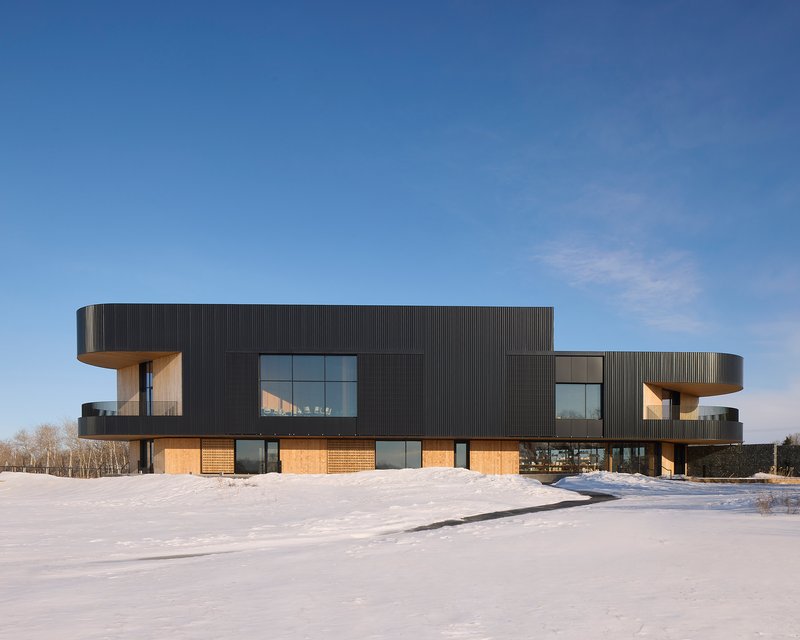 Exterior view showing cantilevered volumes clad in corrugated metal above a timber ground floor in snow