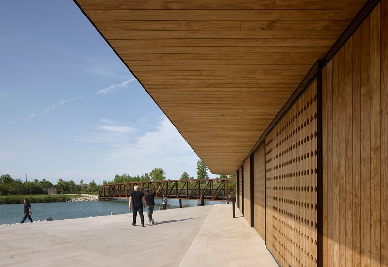 Covered porch with timber soffit and perforated wood screen wall overlooking the pond and steel truss bridge