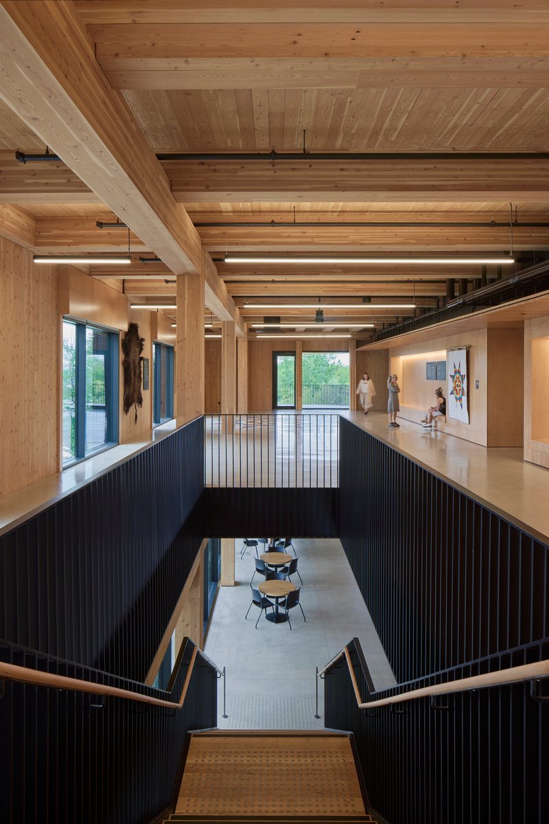 Two-story interior atrium with exposed timber ceiling beams and black vertical railing around central void