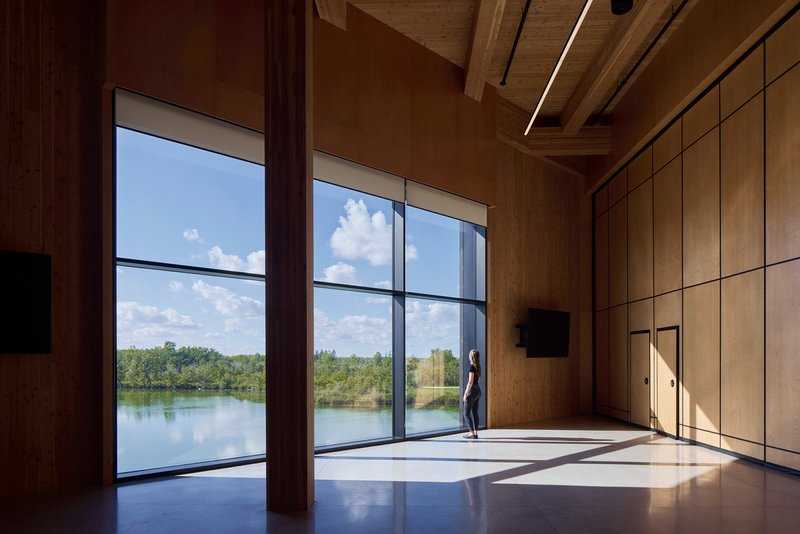 Interior room with floor-to-ceiling windows overlooking a lake under partly cloudy sky