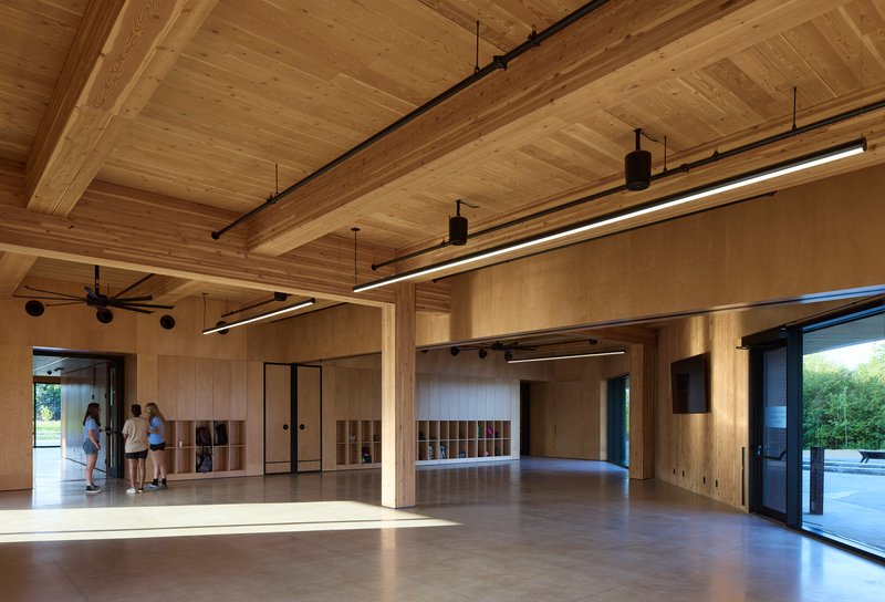 Interior view of open room with timber ceiling, plywood walls, and visitors near sunlit glazing