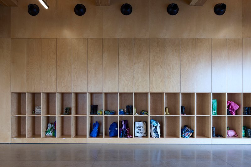 Built-in plywood cubby storage wall with backpacks and bags in individual compartments beneath cylindrical ceiling lights