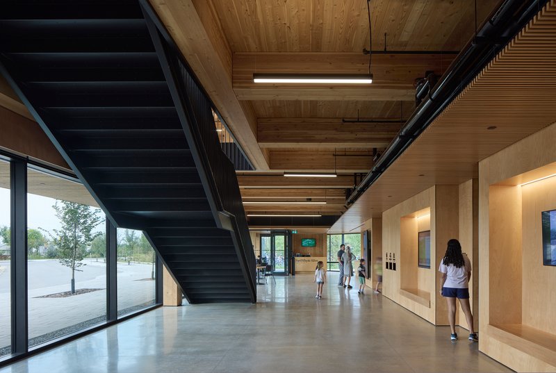 Main circulation corridor with blackened steel staircase ascending beneath exposed timber ceiling structure