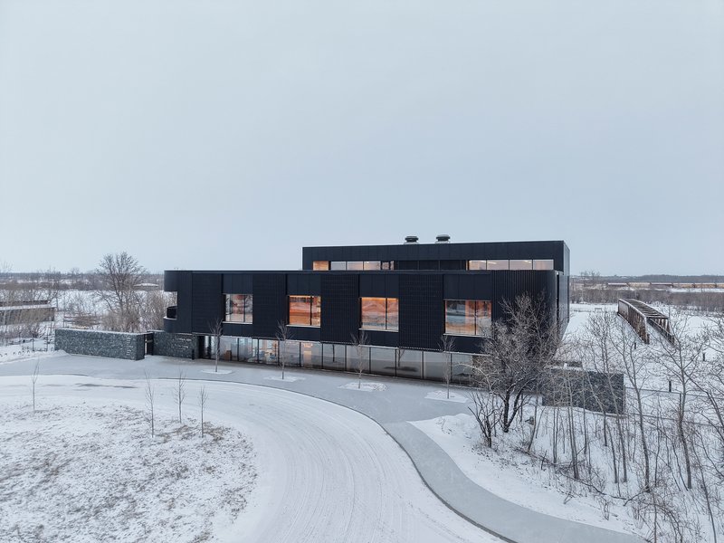 Aerial view showing the black corrugated envelope and curved access drive in a snowy landscape