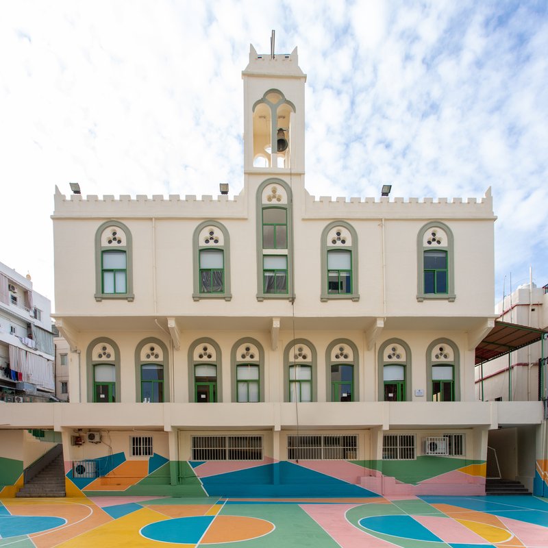 White facade with arched windows and bell tower above a basketball court painted in geometric pastel patterns