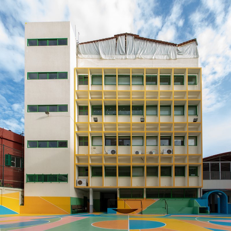 Yellow-framed concrete facade with horizontal windows beside white tower under partly cloudy sky