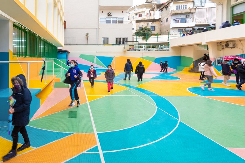 School courtyard with children walking across the colorful geometric sport court patterns on an overcast day