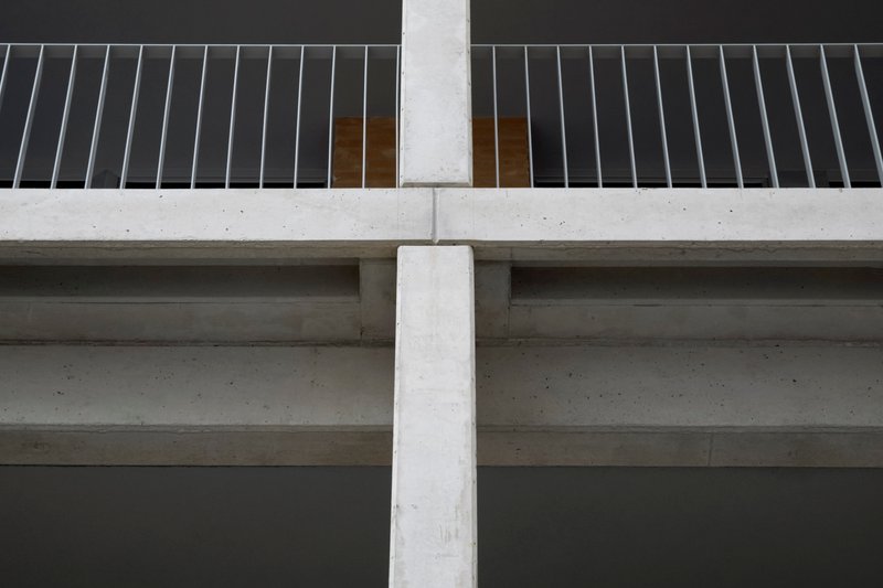 Underside view of concrete balcony slabs meeting a vertical column with vertical metal slat railing above