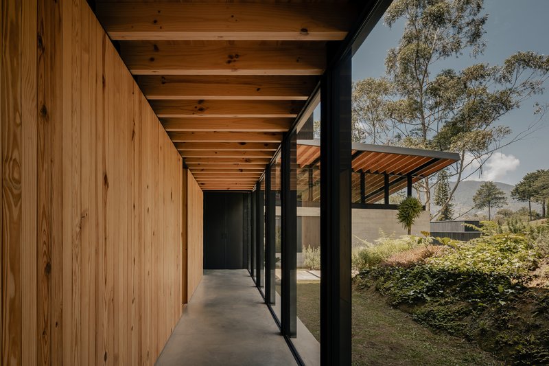 Covered walkway with timber ceiling beams and vertical wood wall alongside planted garden under cloudy sky
