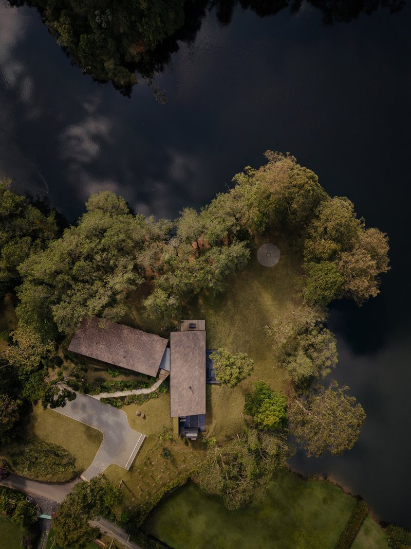Aerial view of three linear volumes on a forested peninsula extending into dark water