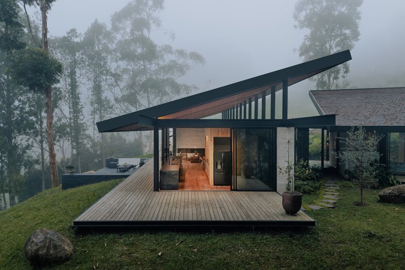Covered timber deck with angled steel-framed roof opening to illuminated interior in mist