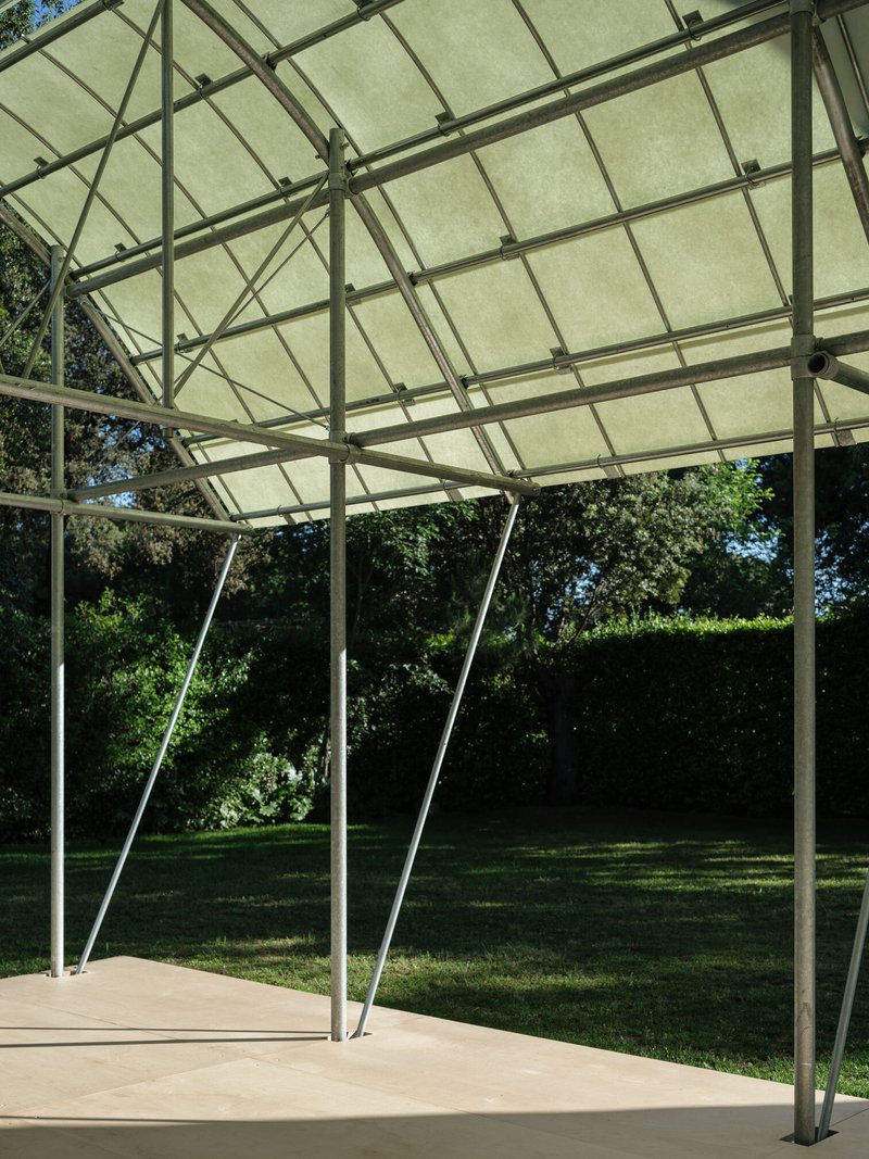 View beneath the tensile canopy showing slender angled steel supports and gridded fabric panels filtering daylight