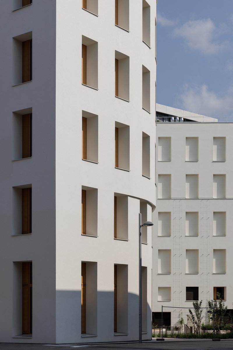 Facade detail showing deep window reveals with timber frames against the white plaster surface