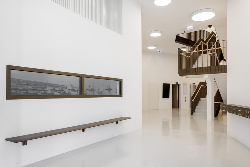Double-height lobby with a timber-clad staircase and circular ceiling lights above polished flooring