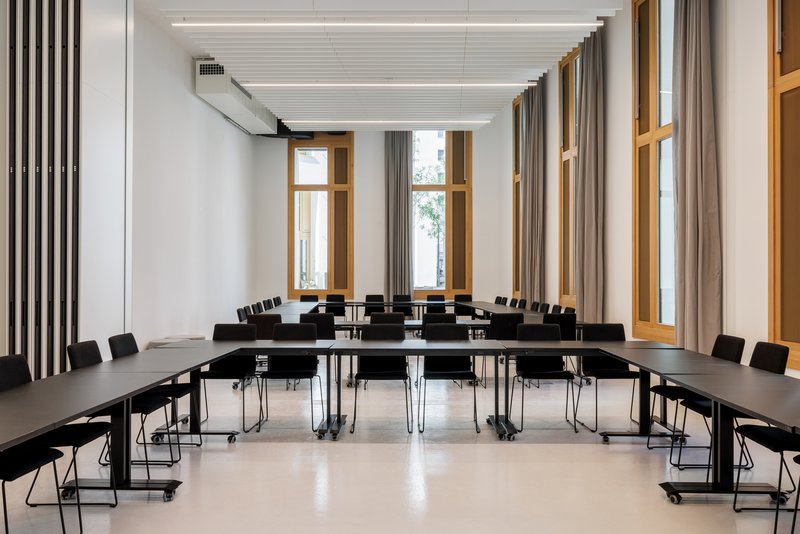 Conference room with black tables and chairs arranged in rows beneath a slatted ceiling