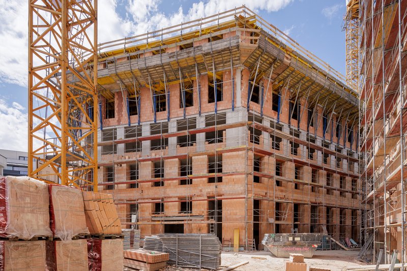 Construction site view of the terracotta block structure with timber framing under yellow tower cranes