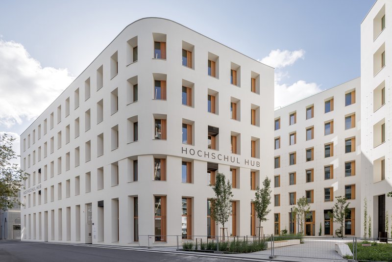 White facade with deep-set timber-lined windows and a ground-level colonnade framing a planted courtyard
