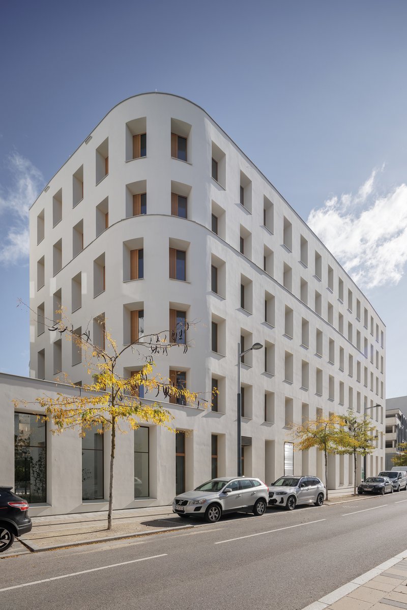 Street view of the curved corner volume with rhythmic window openings and yellow autumn trees