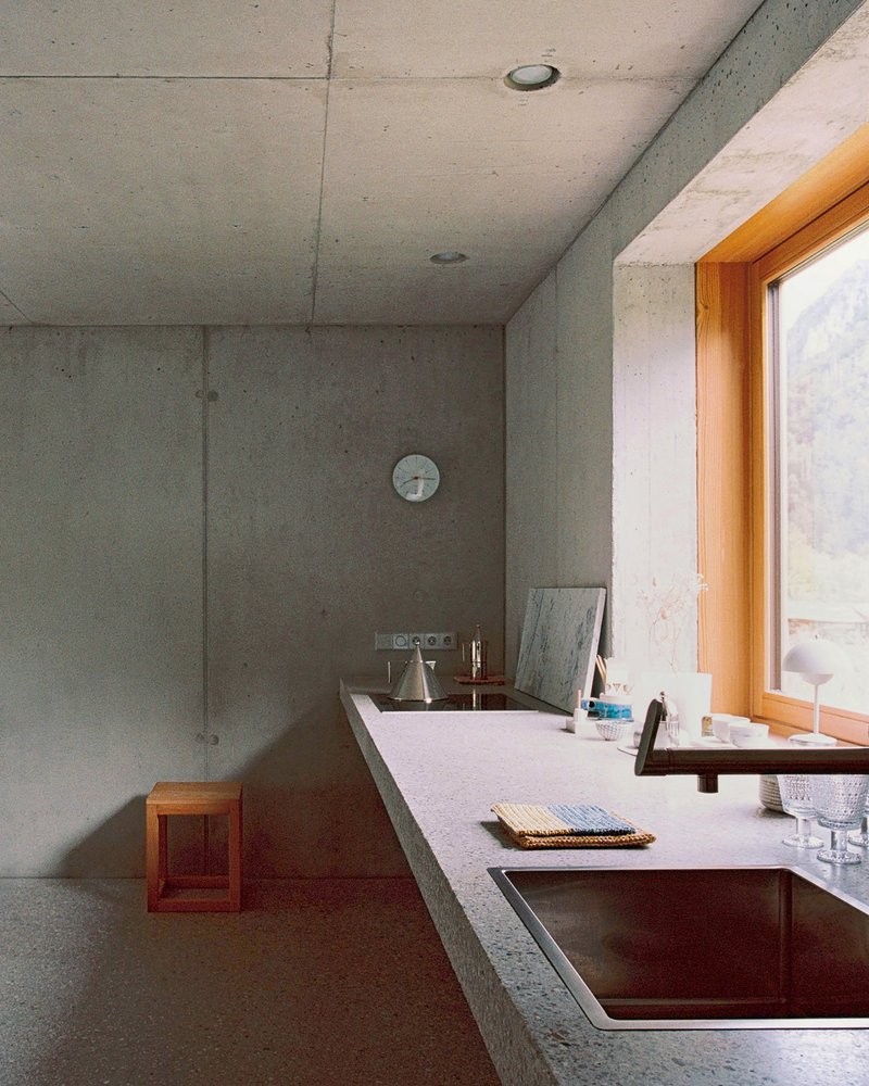 Kitchen with board-formed concrete walls, terrazzo countertop and copper sink beneath a round wall clock