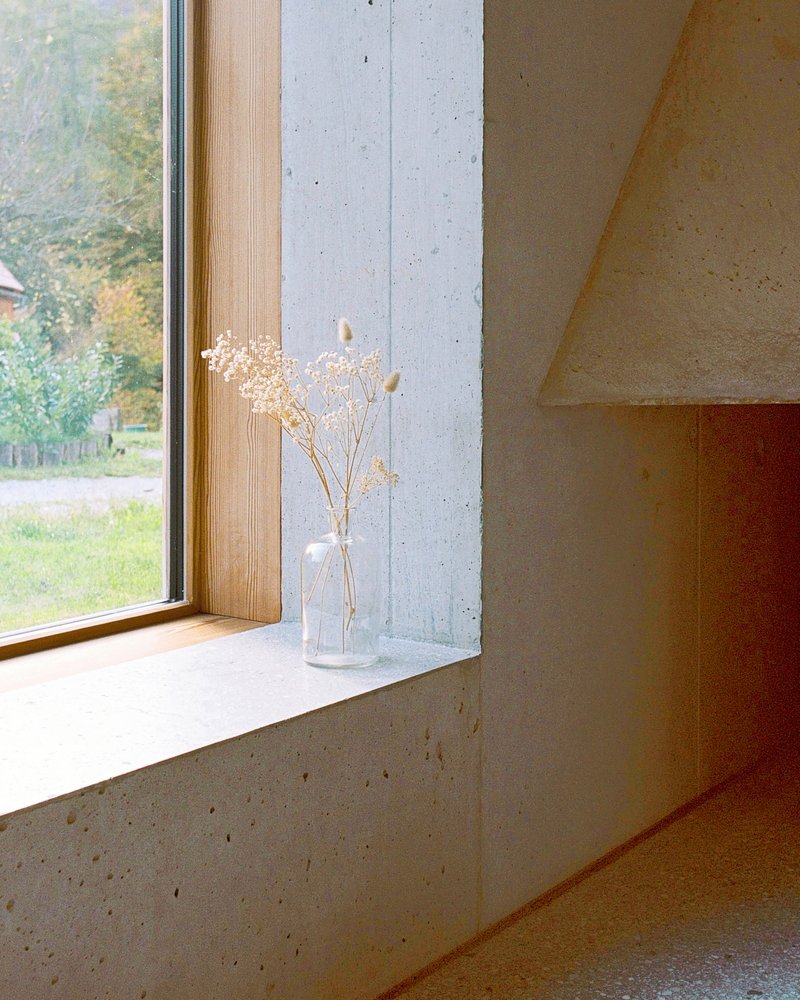 Deep concrete window sill with timber frame holding a glass bottle of dried flowers