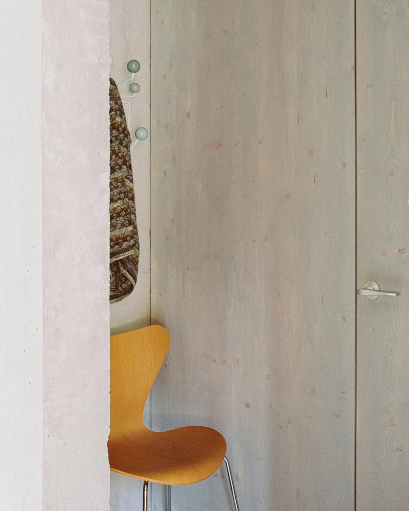 Detail of a plywood door slightly ajar with an orange upholstered chair visible through the opening