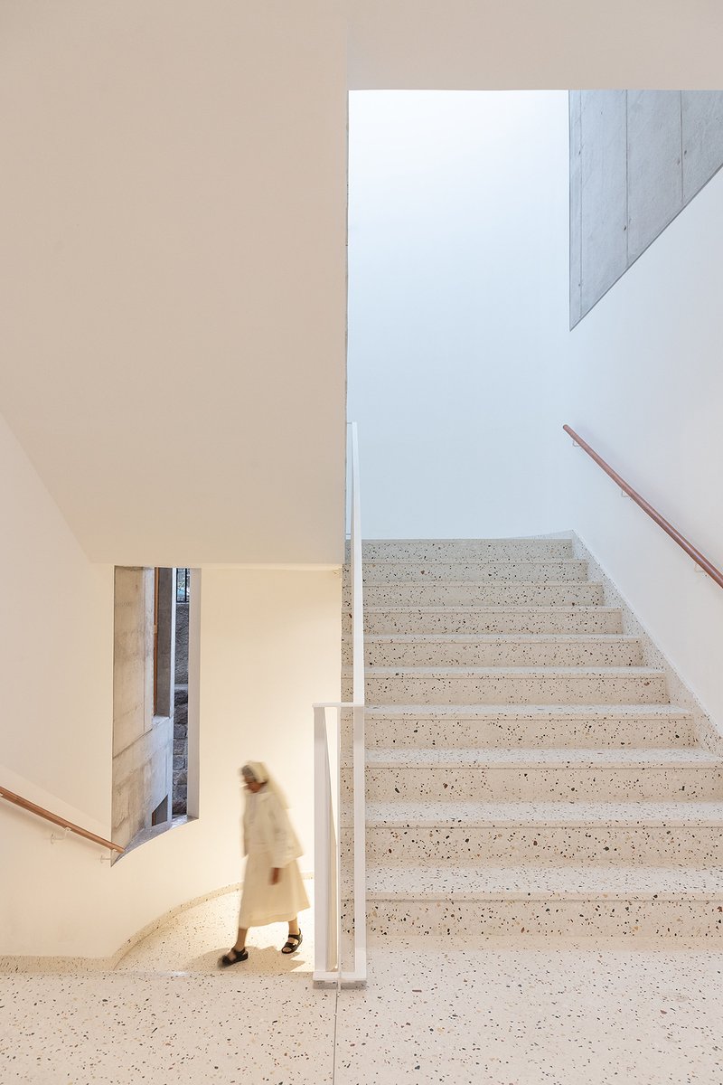 Terrazzo staircase with white vertical slat railing and a person ascending in soft daylight