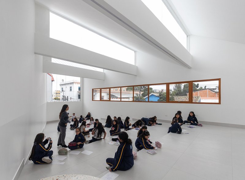 Classroom with continuous timber-framed ribbon windows where students sit on the grey tile floor