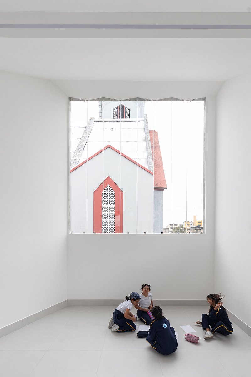 White interior room with students seated on the floor beneath a large window framing a church spire