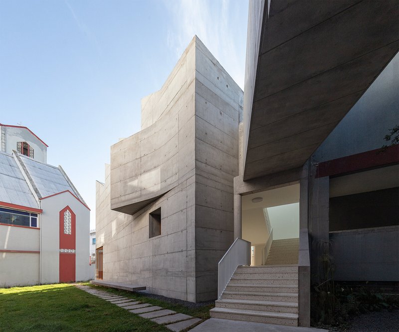 Exterior concrete staircase leading to an entrance beneath a cantilevered volume on a clear day