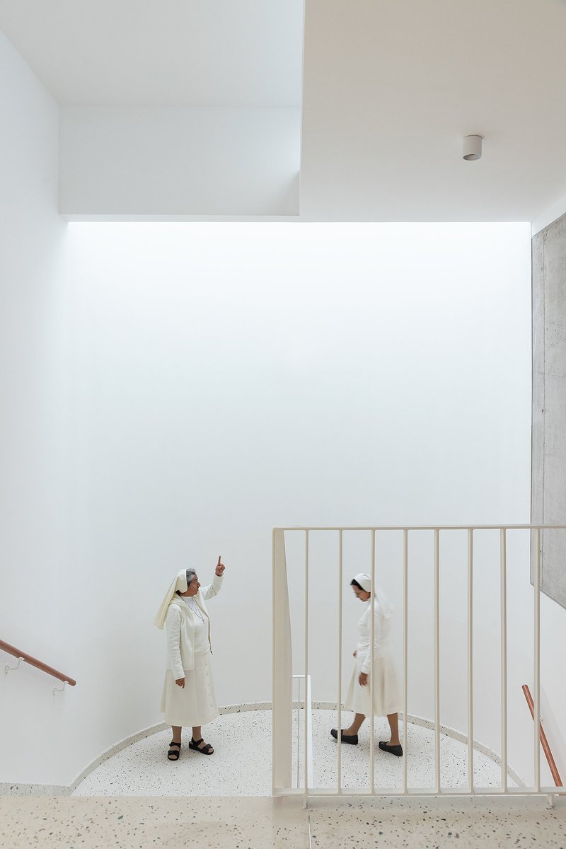 Double-height interior with a curved white balustrade and a person pointing upward in natural light