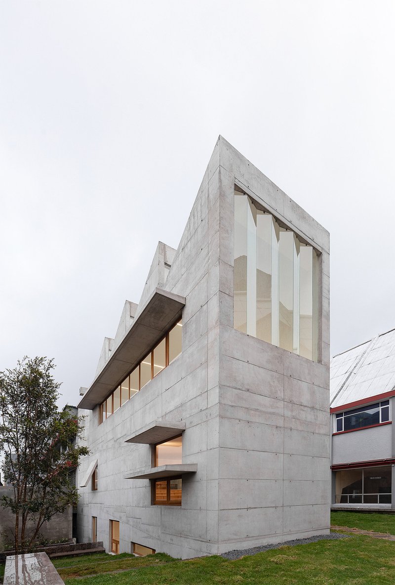 Corner view of the board-formed concrete volume with vertical window openings under overcast sky