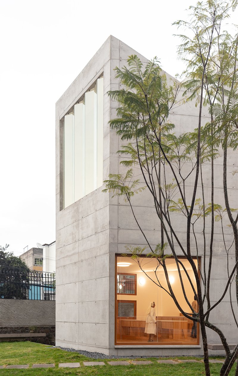 Tall concrete volume with floor-to-ceiling glass and slender trees framed against the facade at dusk