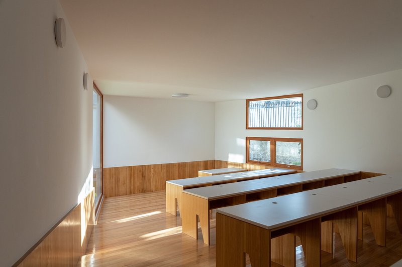 Classroom with timber study tables and wainscoting under bright morning sunlight from corner windows