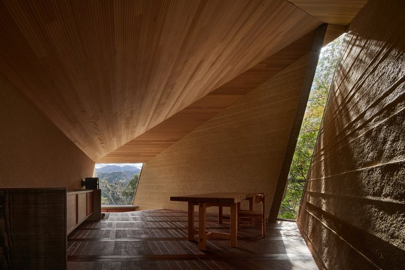 Interior showing ribbed timber ceiling planes converging above stone walls and a framed mountain view