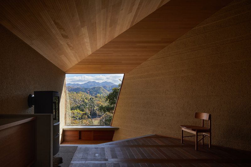 Angled window seat beneath timber ceiling with view to forested hillside and distant peaks