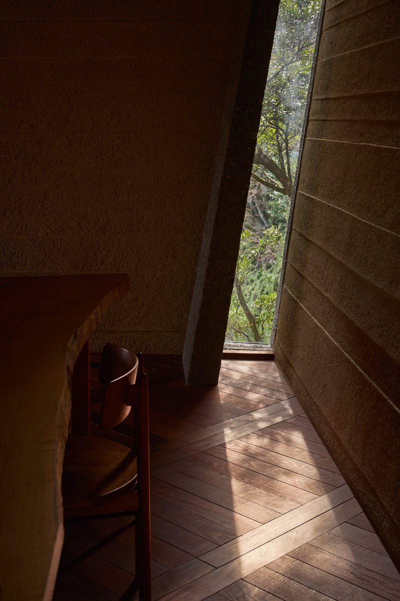 Narrow vertical window slot framing trees between textured stone walls and timber flooring