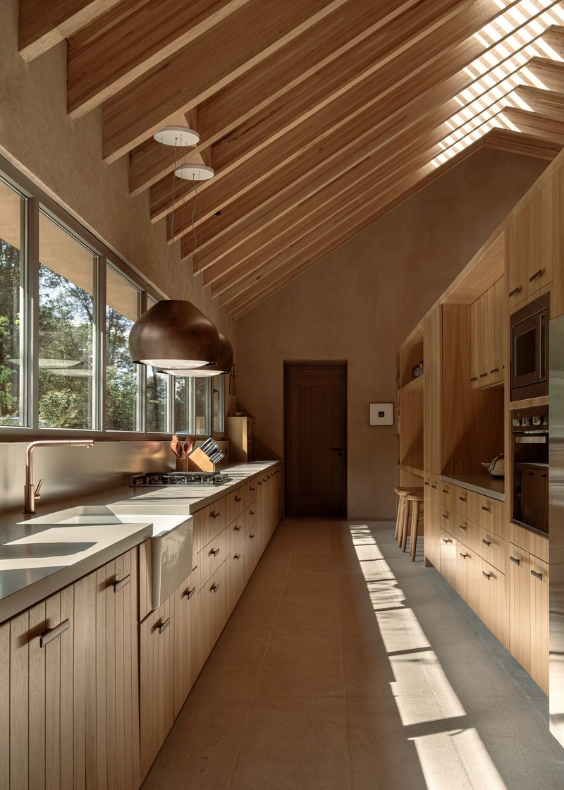 Galley kitchen with timber cabinetry and vaulted ceiling illuminated by slanting afternoon light